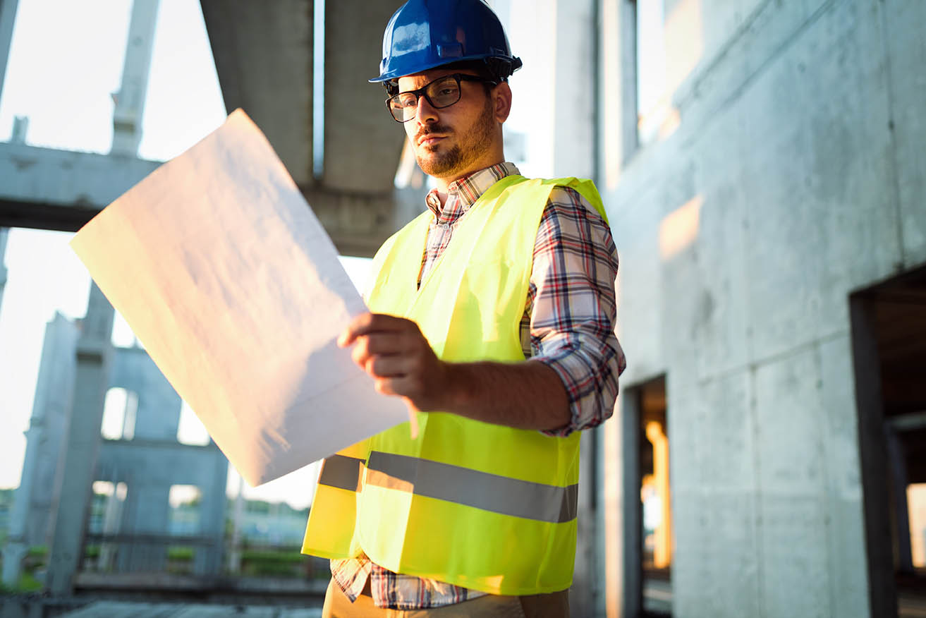 Portrait of male site contractor engineer with hard hat holding blue print paper
